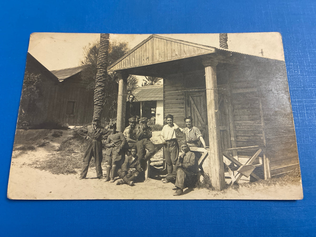 Cartolina postale italiana d'epoca coloniale con soldati e ufficiali del Regio Esercito in posa davanti a un baraccamento militare in legno.