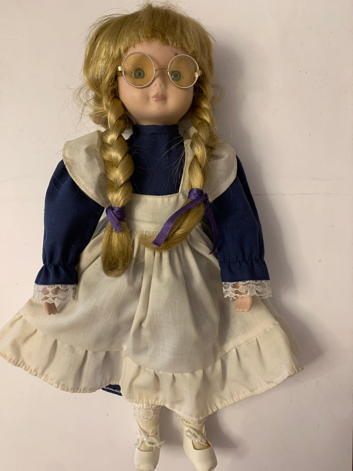 Bambola di porcellana vintage con trecce, occhiali e vestito blu con grembiule